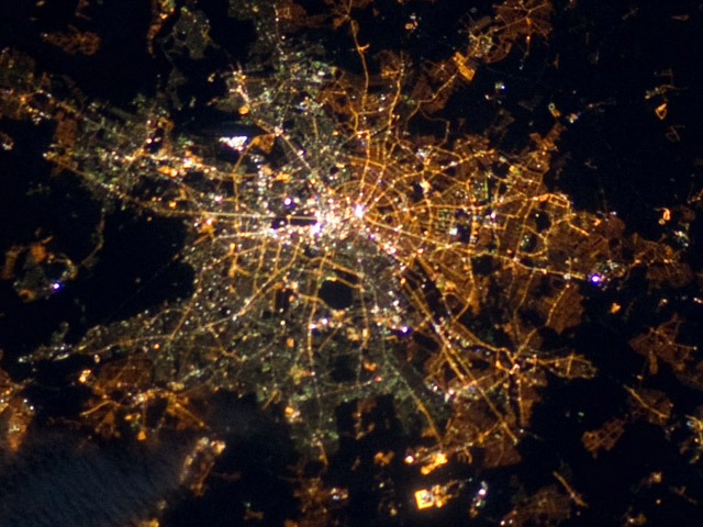 Berlin – geteilt leuchtende Stadt, aufgenommen am 5. April 2012 von der ISS. Die Laternen im Osten der Stadt leuchten gelblich, die Straßenbeleuchtung im Westen ist grünlich. Quelle: NASA (public domain).